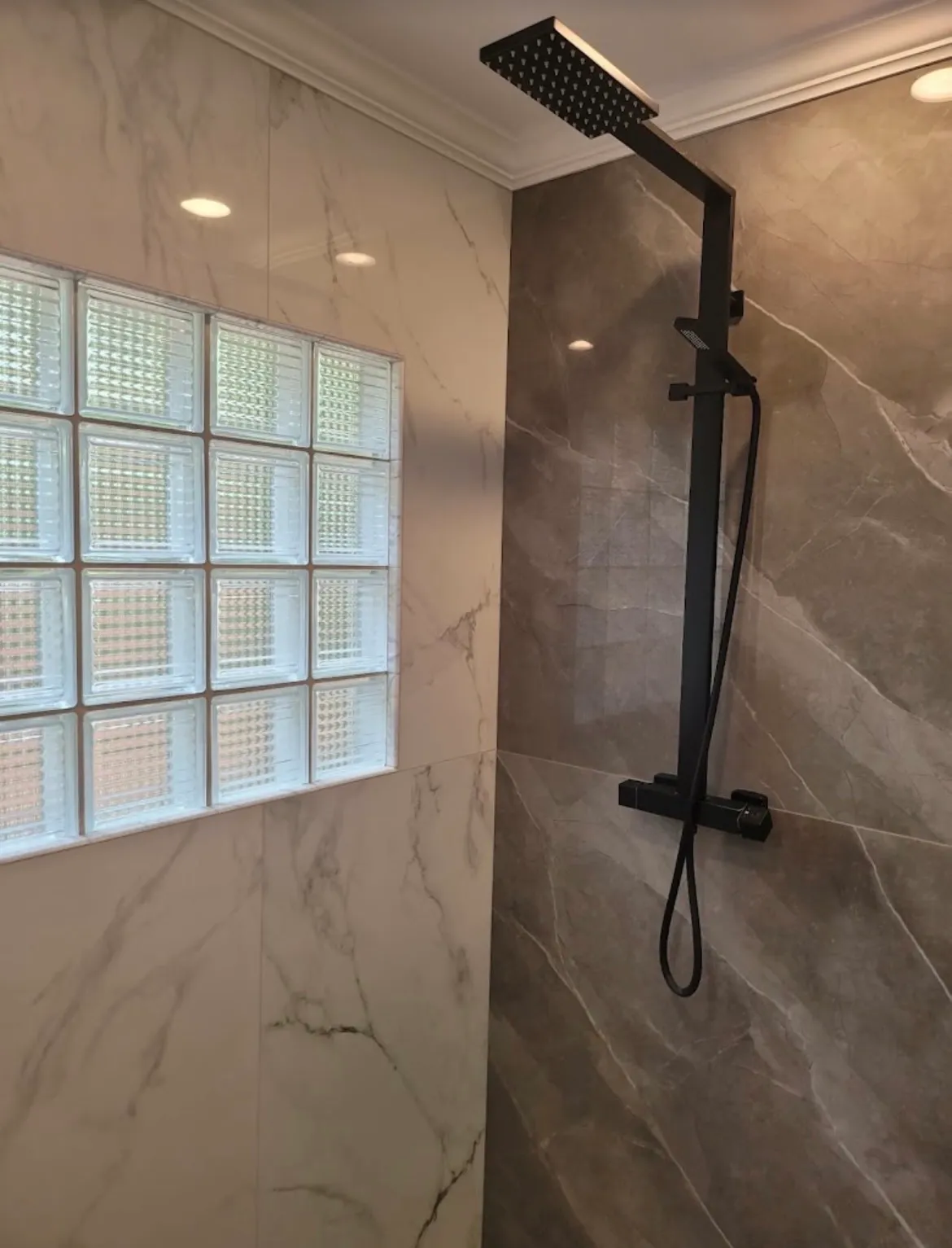 Large-format marble-look shower tile with matte black rain shower and glass block window