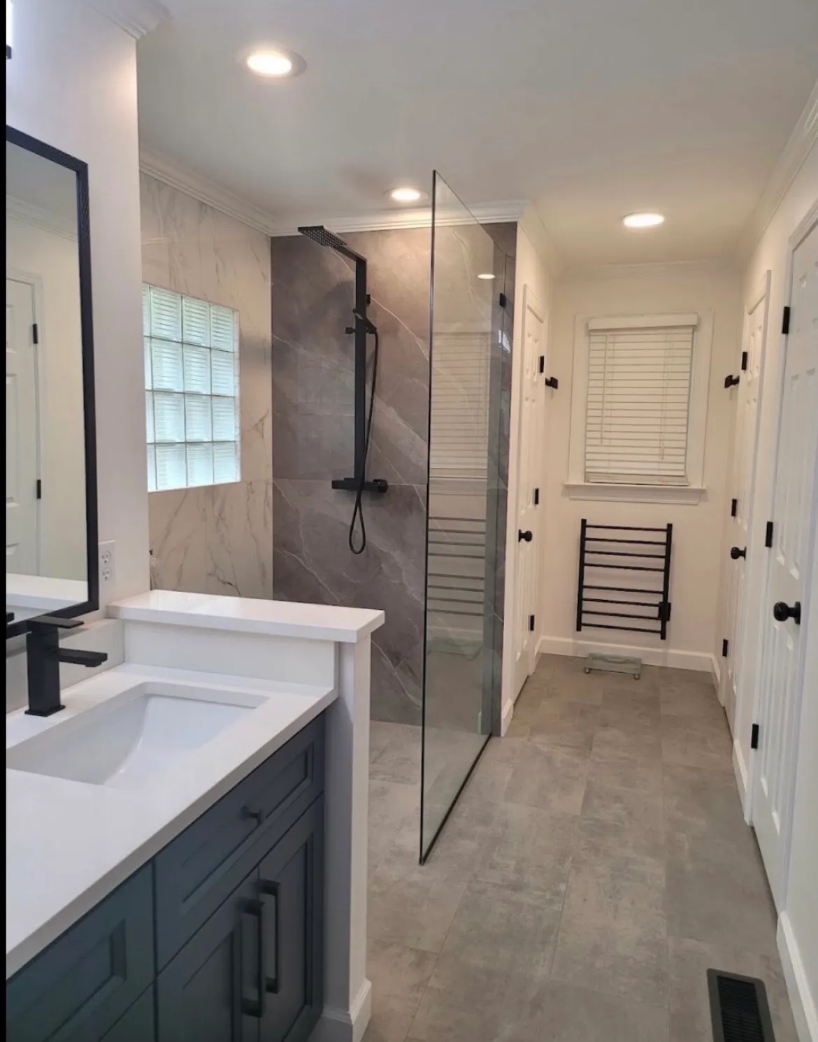 Modern bathroom remodel with navy vanity, gray floor tile, and frameless glass shower